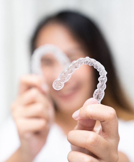 Closeup of smiling patient holding clear aligners