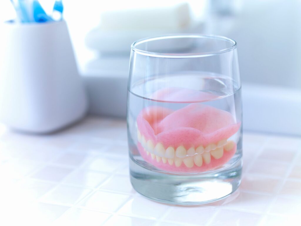 Full set of dentures in a glass of clear liquid on tiled surface