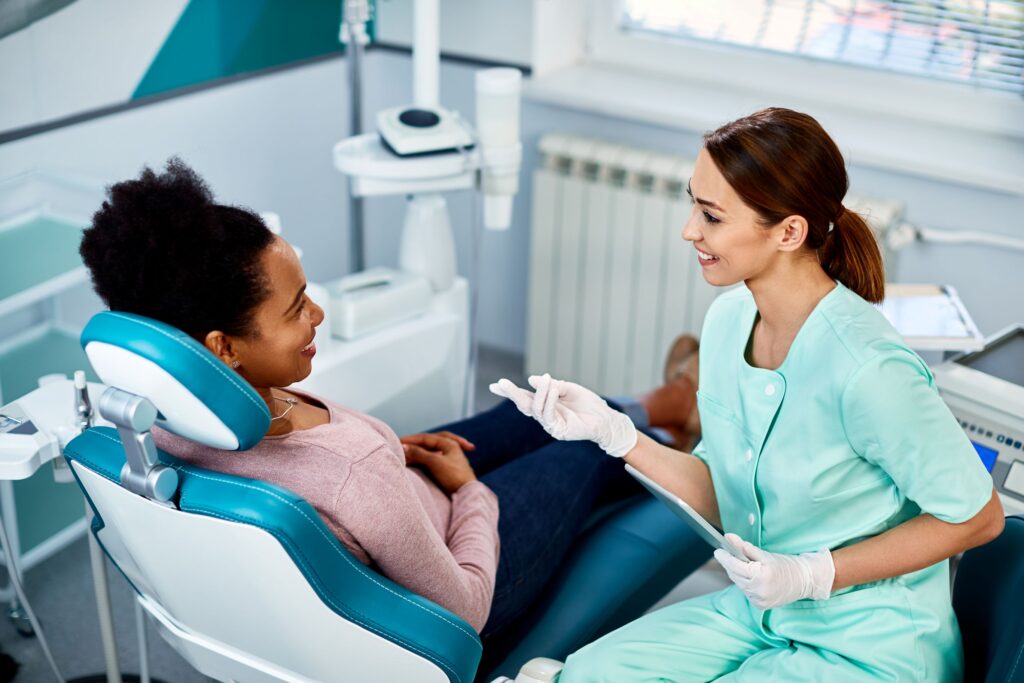 Dentist in green scrubs speaking with woman in dental chair